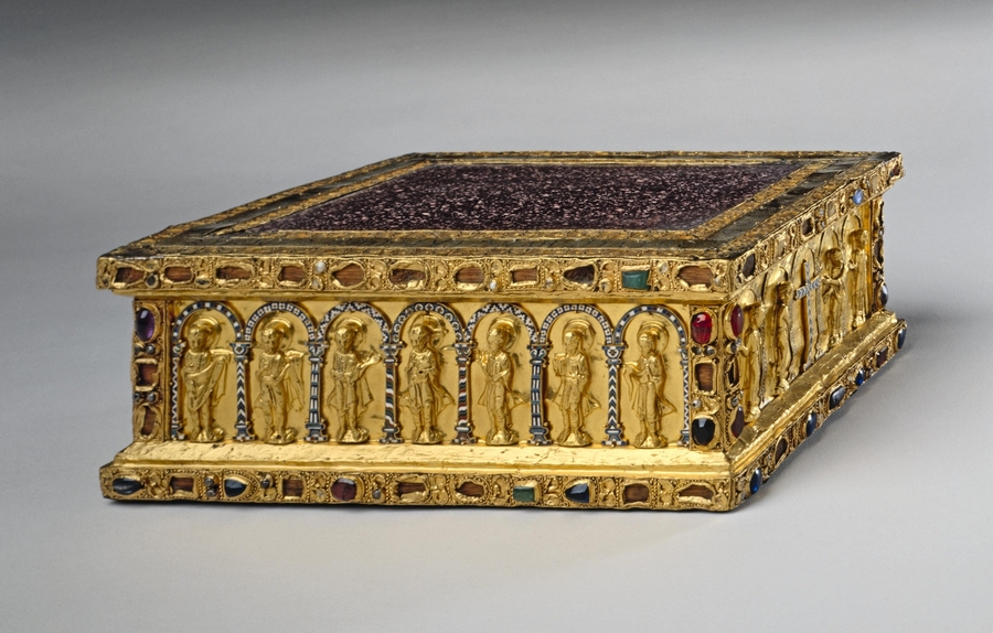 A gem-encrusted gold altar is a squat rectangular box with a white-speckled porphyry top. Archangels, apostles, and Christ are shown within a colonnade depicted on the object's sides. 