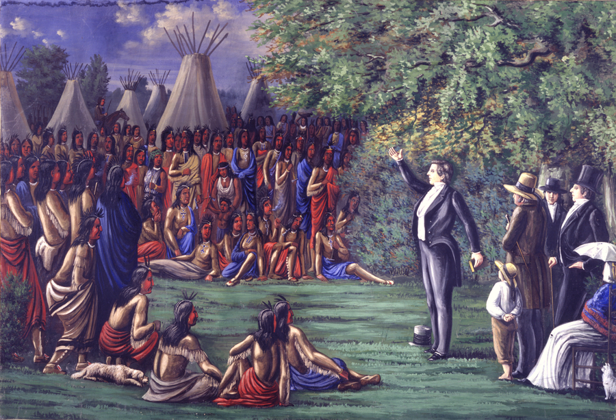 In this painting, a light-skinned man in a black waistcoat raises his hand and addresses a large assembly of figures. They wear stereotypical American Indian dress of hide clothes and red or blue cloaks. Teepees stand in the background.